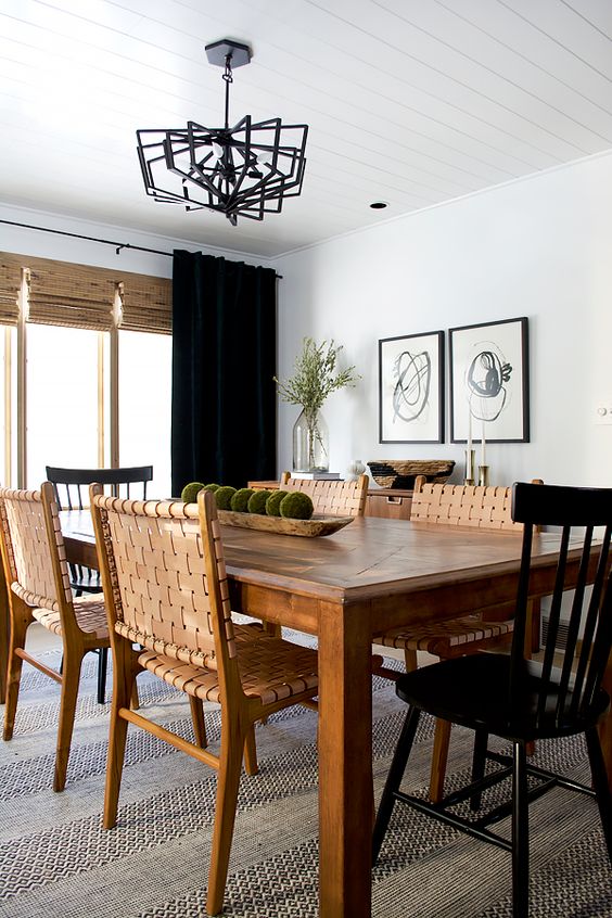 a contrasting modern farmhouse dining room with a stained table, woven leather and black wooden chairs, a mini gallery wall and curtains