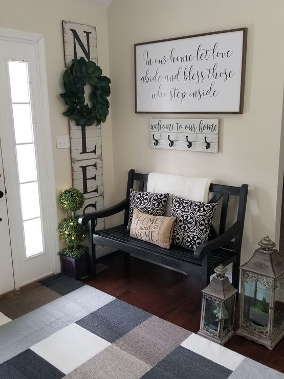 a cozy famrhouse entryway with a blakc vintage bench, candle lanterns, a sign and a colored rug