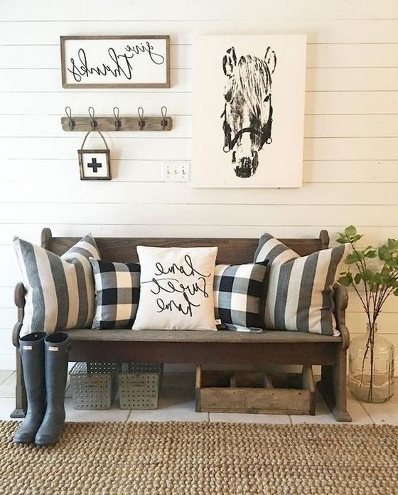 a cozy farmhouse entryway with a dark stained bench, printed pillows, some artworks and a large jute rug