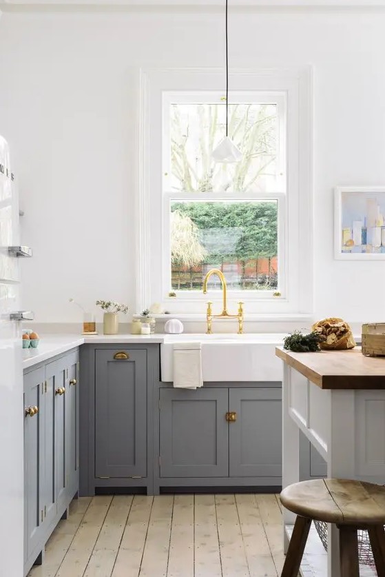 a cozy farmhouse kitchen with grey shaker cabinets, white countertops, a white kitchen island with a butcherblock countertop and pendant lamps