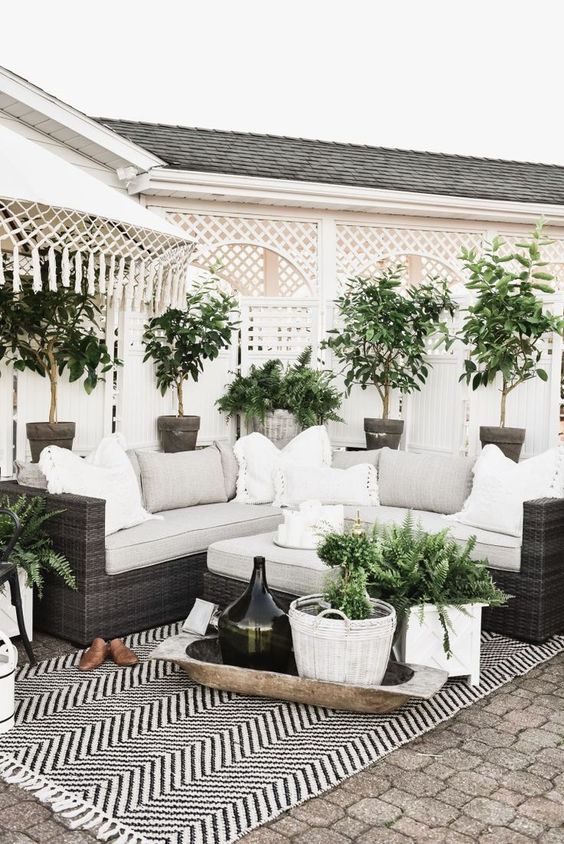 a cozy farmhouse patio with a black wicker sofa and neutral pillows and potted greenery around is a lovely and welcoming space
