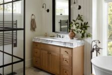 a cozy modern farmhouse bathroom with shiplap walls, a shower space, a vanity and a mirror, a tub, a wooden stool and a boho rug