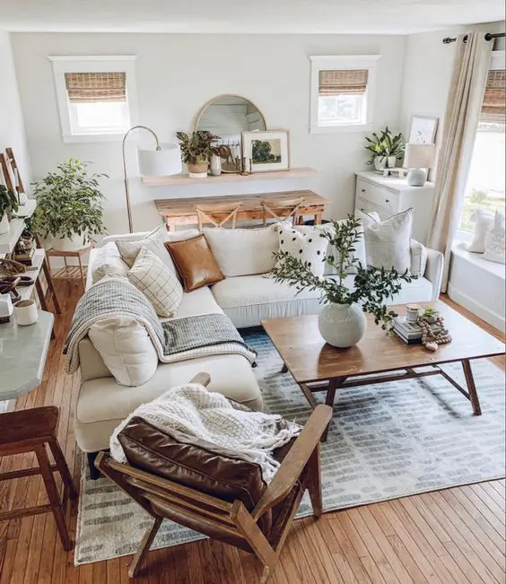 a cozy modern farmhouse living room with a console and chairs, a shelf with a mirror, a dresser, a white sectional, some tables and a leather chair