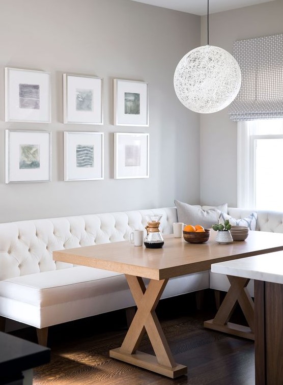 a cozy neutral farmhouse dining space with a creamy sectional, a stained trestle dining table and a gallery wall, a pendant lamp