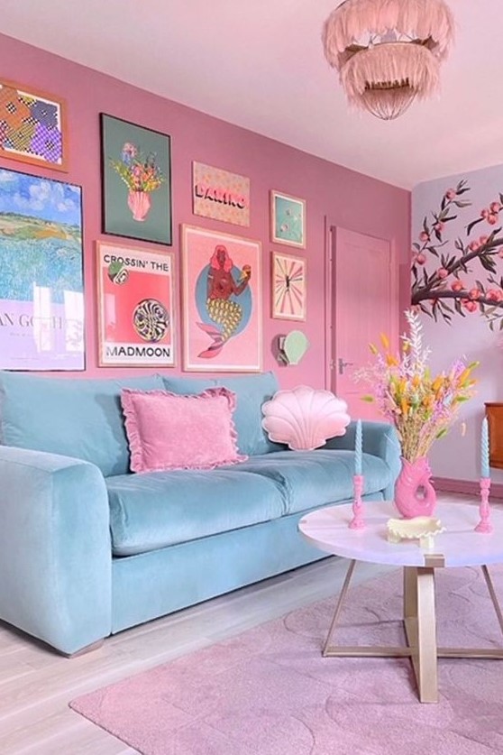 a cute living room with a mauve accent wall, a blue sofa and pink pillows, a bright gallery wall, a pink rug and a chandelier