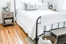 a dreamy farmhouse bedroom with a forged bed, wooden nightstands, a wooden bench and a basket for storage, some greenery
