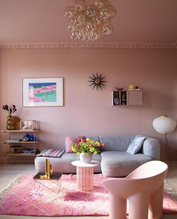 a dusty pink living room with a low grey sofa, a tiered shelf, some sculptural furniture and bright accents