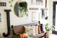 a fall farmhouse entryway with a wooden bench, some racks and shelves, a gallery wall and lots of pumpkins