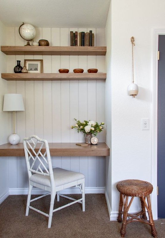 A farmhouse home office nook with built in shelves and a desk, a white chair, a woven stool and some decor and books