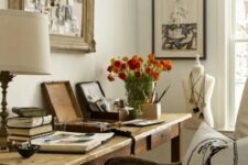 a farmhouse home office with a wooden desk, a refined chair, chic artworks and a table lamp and blooms