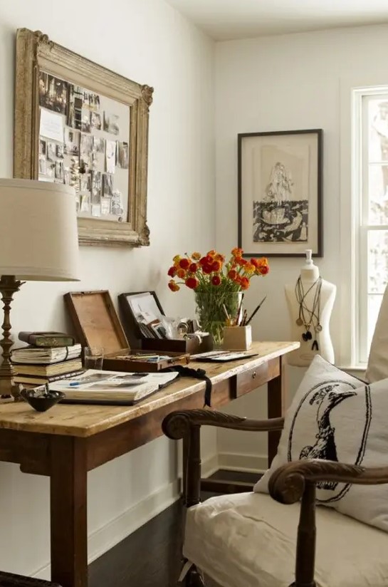 a farmhouse home office with a wooden desk, a refined chair, chic artworks and a table lamp and blooms