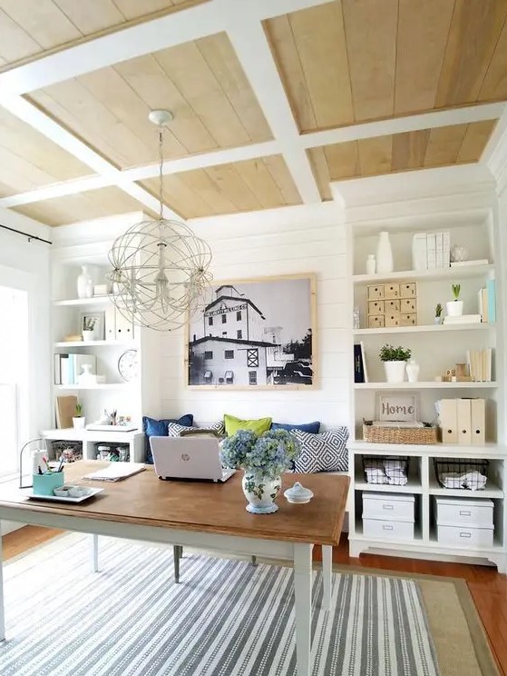 A farmhouse home office with built in storage units, a simple desk and a built in bench to sit on, a sphere chandelier