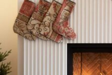 a fireplace clad with a reeded surround, with a bold artwork over it and some stockings and candles to style it for Christmas