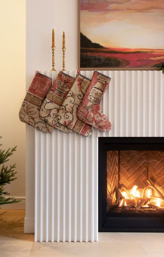 a fireplace clad with a reeded surround, with a bold artwork over it and some stockings and candles to style it for Christmas