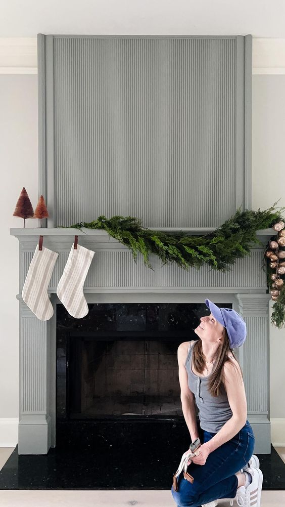 a fireplace with a grey reeded surround and a mantel, decorated for Christmas with stockings, bottlebrush trees and an evergreen garland