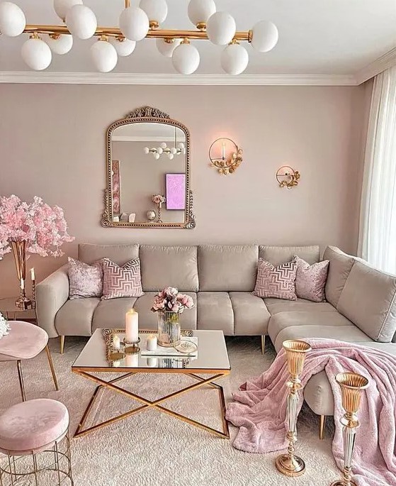 a glam living room with dusty pink walls and a matching sectional sofa, pink pillows and blankets, pink blooms, poufs and chairs and some mirrors