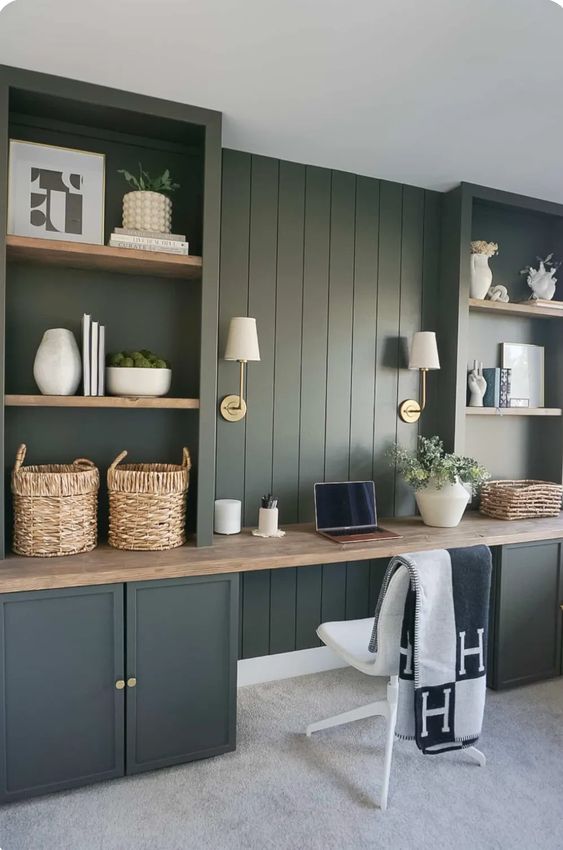 a green modern farmhouse home office with shiplap walls and storage units, a butcherblock countertop, sconces and greenery