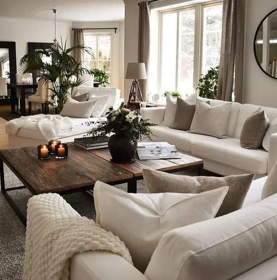 a grey living room with creamy sofas and a lounger, taupe and creamy pillows, taupe curtains, a duo of rich-stained coffee tables