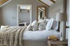 a grey modern farmhouse bedroom with wooden beams, a large upholstered bed with neutral bedding, a wooden chest