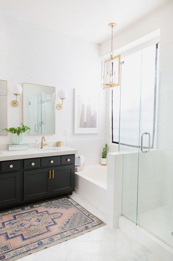 A light filled farmhouse bathroom with a black vanity, gilded touches, white tiles and lamps