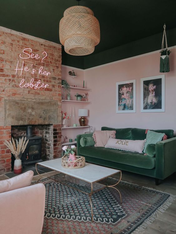 a light pink living room with a hearth, built-in shelves, a green sofa, a blush chair, neon lights and some artwork