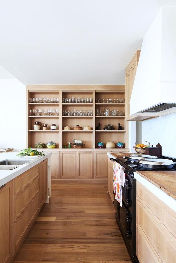 A light stained wooden kitchen with wooden countertops, built in wooden storage units and a white hood is very welcoming
