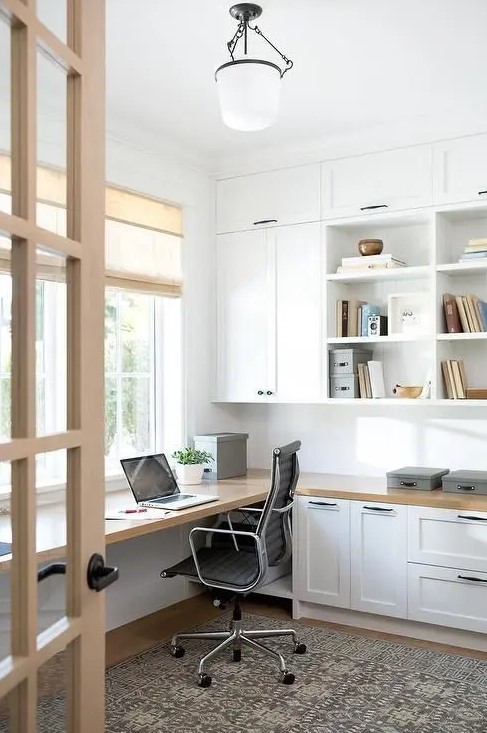 a lovely modern country home office with white kitchen cabinets used for storage, a floating desk and some simple shades plus a vintage lamp