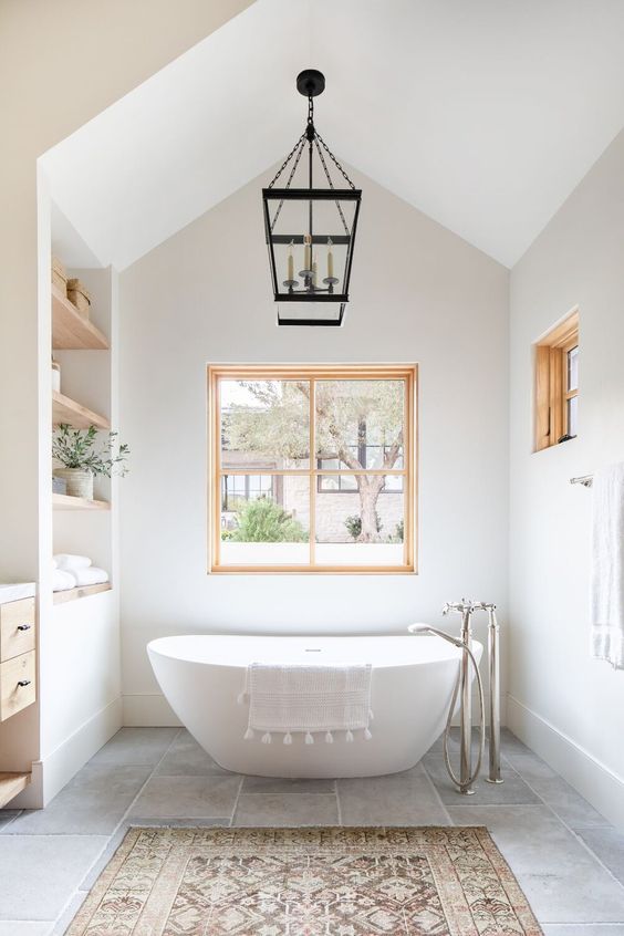 a lovely modern farmhouse bathroom with built-in shelves, a timber vanity, an oval tub, a couple of windows with stained frames