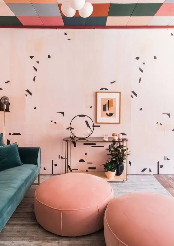 a lovely pink living room with a colorful ceiling, printed walls, a green sofa, pink ottomans and potted plants