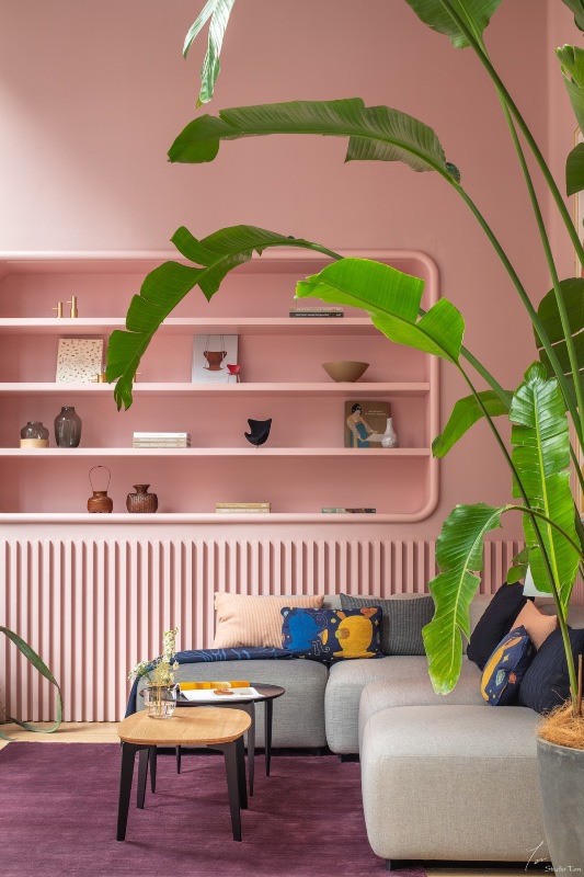 a lovely pink living room with niche shelves, a fluted detail, a grey sectional, a couple of coffee tables and a mauve rug