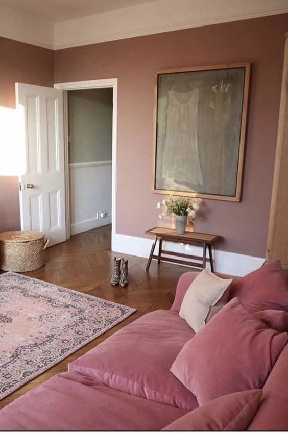 a mauve living room with a pink sofa, a vintage artwork, a bench, a pink printed rug, a basket with a lid