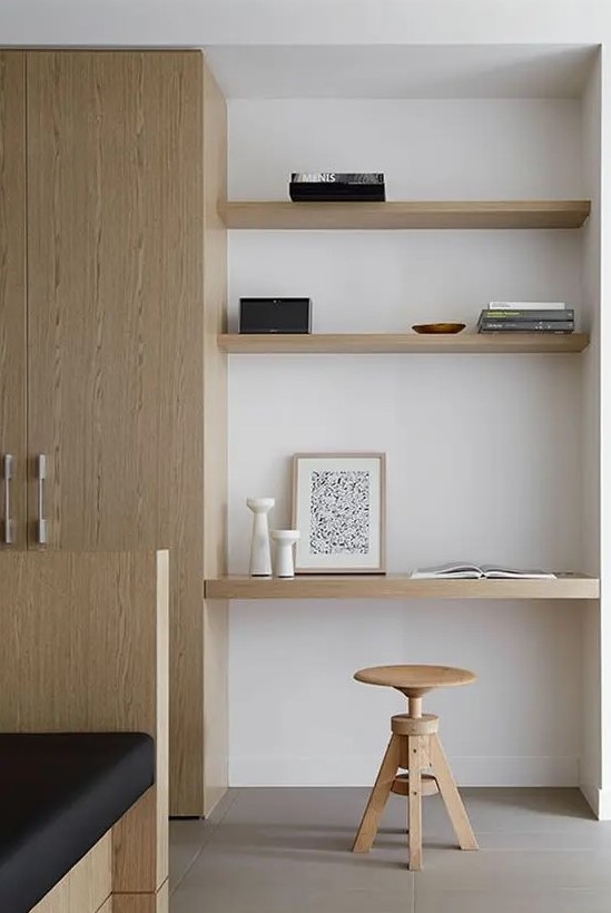 A minimalist awkward nook with built in shelves and a desk, with a wooden stool and books plus candle lanterns is amazing