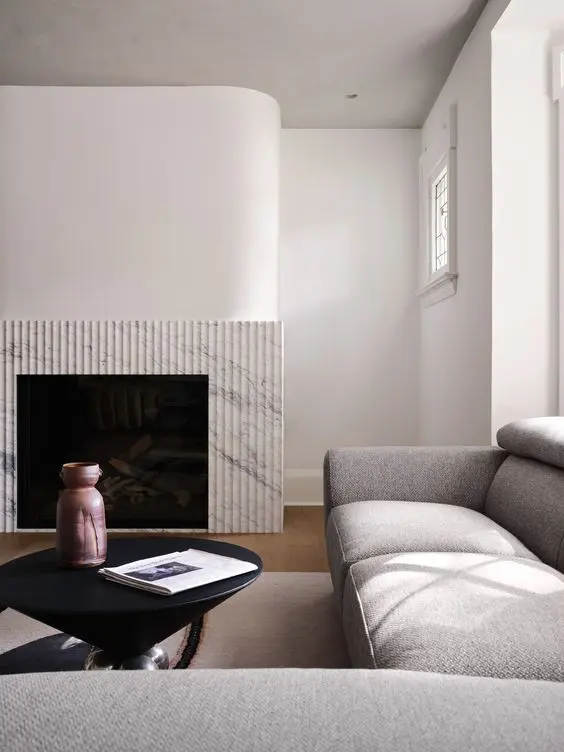 a minimalist space with a fireplace with a fluted surround, a large grey sectional and a black coffee table with decor