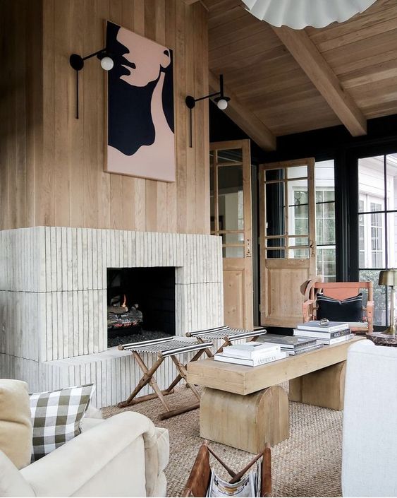 a modern chalet space with a fluted fireplace, folding stools, a coffee table and neutral chairs, some decor