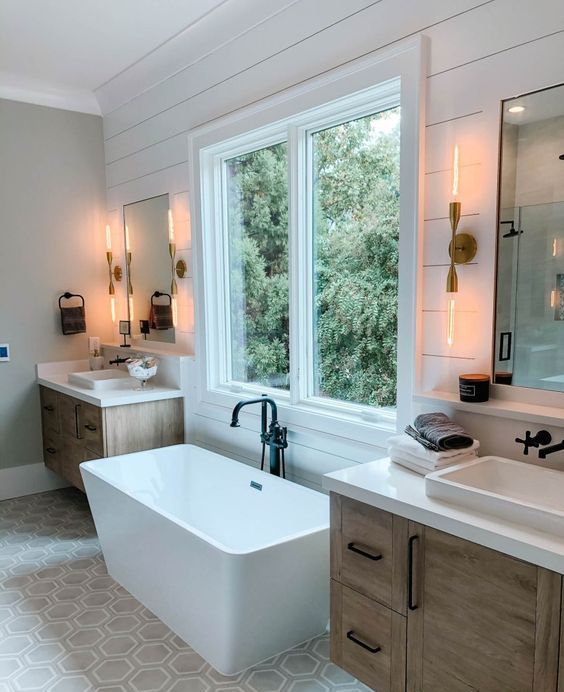 a modern cottage bathroom with shiplap on the walls, a geo tile floor, stained vanities, a square tub by the window