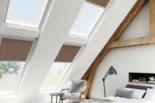 a modern country bedroom with an attic ceiling and lots of windows, wooden beams and a built-in fireplace, cool furniture and a sitting nook by the window