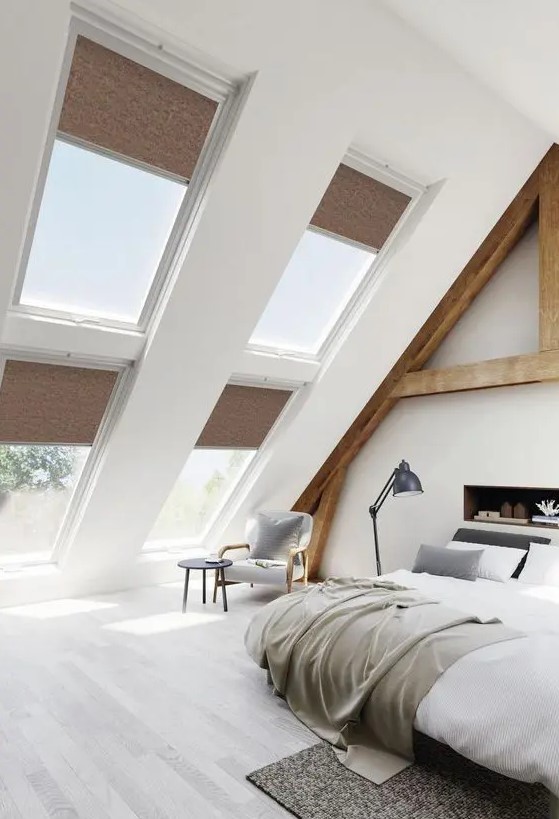 A modern country bedroom with an attic ceiling and lots of windows, wooden beams and a built in fireplace, cool furniture and a sitting nook by the window