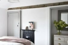 a modern country bedroom with dark stained wooden beams, a non-workign fireplace, neutral furniture and neutral textiles