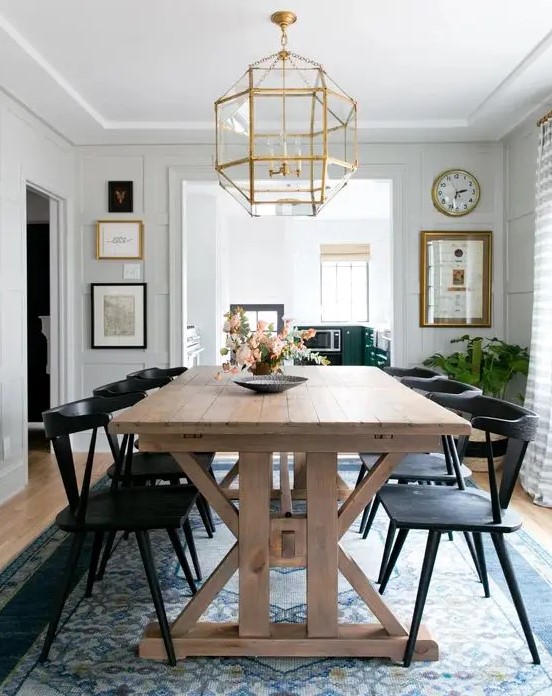 a modern country dining space with a stained trestle dining table, black chairs, a blue rug and a gilded faceted chandelier