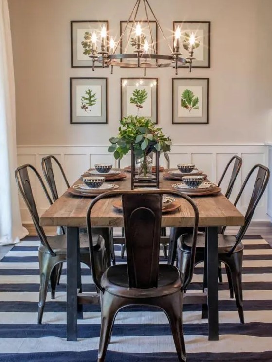 a modern country dining zone with a stained table, metal chairs, a striped rug, a large metal chandelier and an organic gallery wall