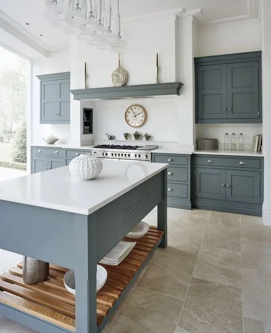 A modern country kitchen with graphite grey cabinets and a kitchen island, white countertops and a built in hood plus a glazed wall