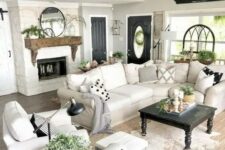 a modern country living room with a fireplace, chic neutral furniture, printed pillows, a wooden mantel and potted plants