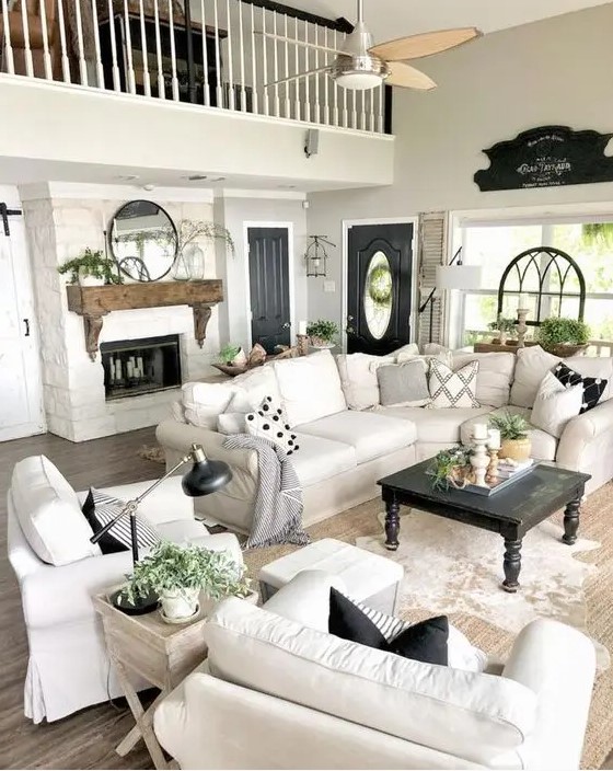 a modern country living room with a fireplace, chic neutral furniture, printed pillows, a wooden mantel and potted plants