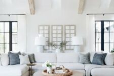a modern country living room with wooden beams on the ceiling, neutral furniture, printed pillows and a round table is welcoming