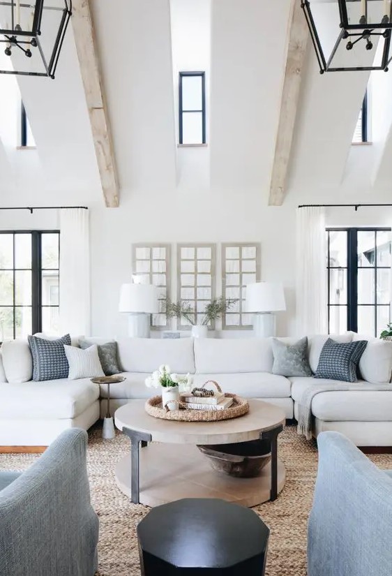 a modern country living room with wooden beams on the ceiling, neutral furniture, printed pillows and a round table is welcoming