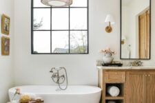 a modern country meets boho bathroom with a window, an oval tub, a timber vanity, a boho rug, a wooden stool and a pendant lamp