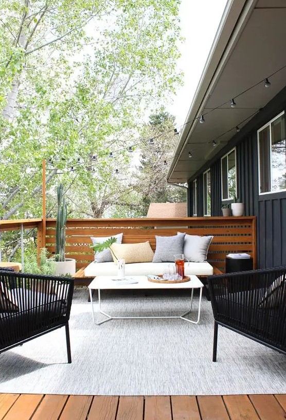 a modern country terrace with a wooden deck, a large rug, a sofa, rattan chairs, a small table and potted plants and cacti