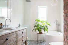 a modern farmhouse bathroom with a printed tile floor, a stained wooden vanity, a brick wall and a potted plant
