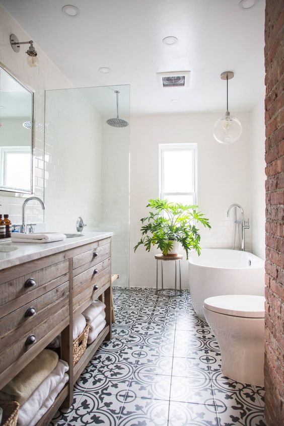 a modern farmhouse bathroom with a printed tile floor, a stained wooden vanity, a brick wall and a potted plant
