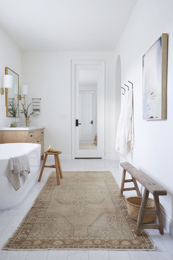 a modern farmhouse bathroom with an oval tub, a timber vanity, a wooden stool and a bench, some artwork